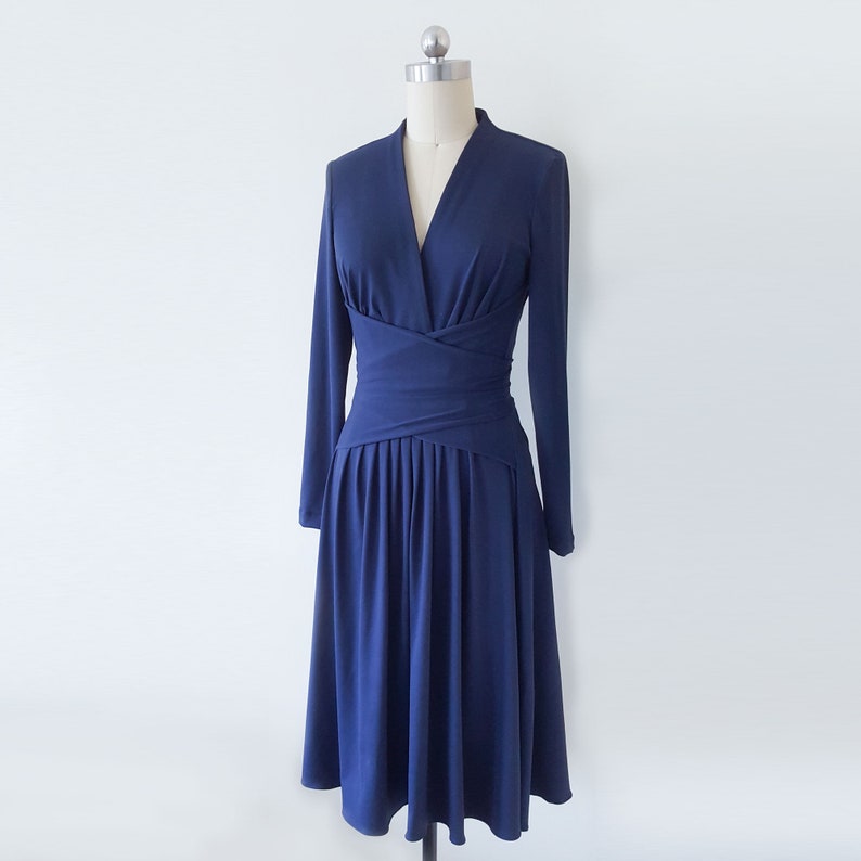 May include: A navy blue long-sleeved dress with a V-neckline and a wrap-style bodice. The dress has a fitted waist and a flowing skirt.