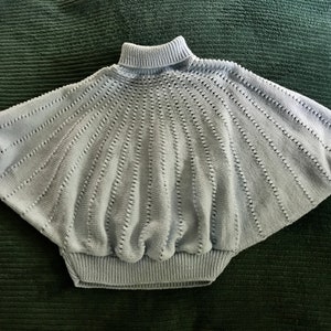 May include: A light blue knitted sweater with a turtleneck and a loose, flowing fit. The sweater has a delicate, open-stitch pattern.