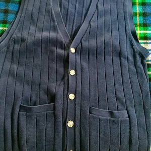 May include: A navy blue knitted vest with a V-neck, six gold buttons, and two pockets. The vest is ribbed and has a casual style.