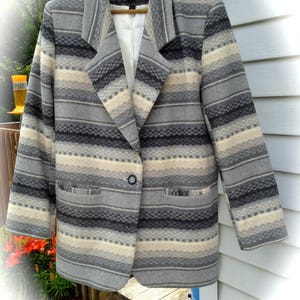 May include: A gray, white, and black striped blazer with a single button closure. The blazer has a collar and two pockets. The label on the blazer reads "Brattan".