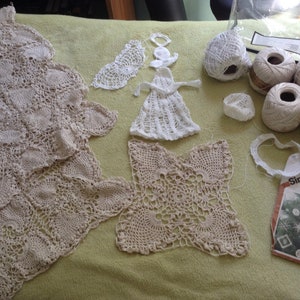 May include: A collection of white crocheted doilies, including a large doily, a smaller doily, and a doily shaped like an angel. There are also balls of white yarn and a Simplicity pattern for crocheting snowflakes and a Christmas tree.