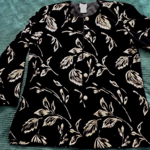May include: A black velvet jacket with a gold floral pattern. The jacket has a button closure and long sleeves.