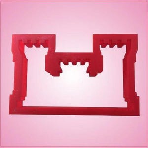 May include: A bright red castle-shaped cookie cutter. The cutter has a rectangular base with two castle towers on either side and a smaller central section. The design is detailed with crenellations along the top edges.