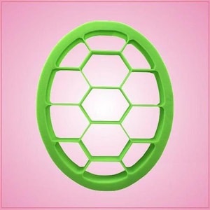 May include: A bright green, oval-shaped cookie cutter with a soccer ball design. The cutter features a series of interconnected hexagons and curved edges, creating the pattern. The cutter is made of plastic and is set against a pink background.
