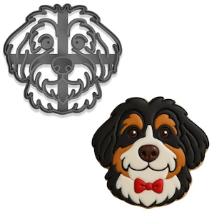 May include: A gray plastic cookie cutter in the shape of a Bernese Mountain Dog's head is next to a decorated cookie. The cookie has black, brown, and white icing, with a red bow tie. The cookie is a detailed replica of the dog's face.