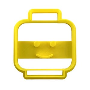 Puede incluir: Un cortador de galletas amarillo brillante con forma de cara sonriente. El cortador tiene un contorno rectangular con un asa en la parte superior y una barra horizontal con dos ojos circulares y una boca curva.