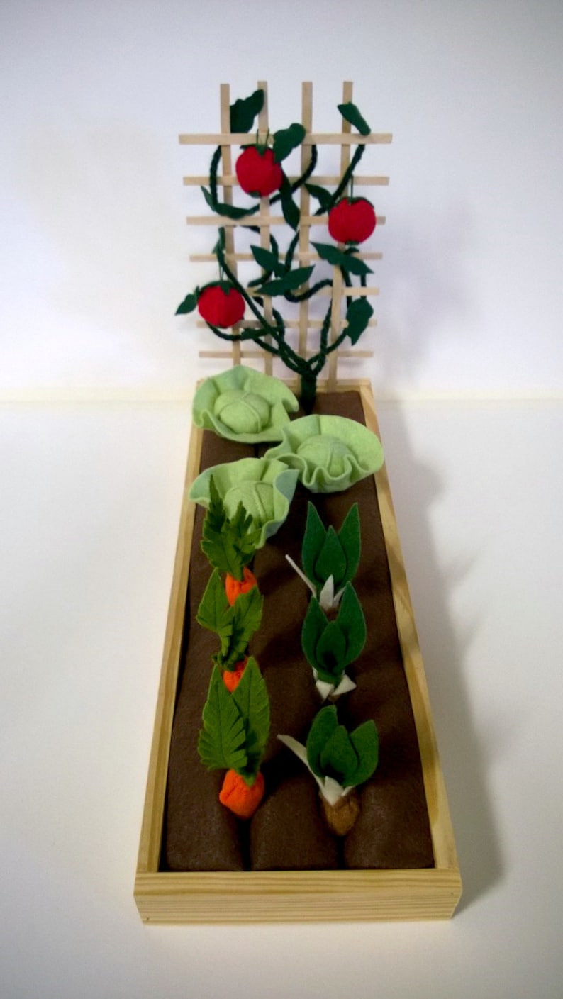May include: A wooden planter box with brown felt lining. The planter contains felt representations of a tomato plant with red tomatoes, two heads of cabbage, and three rows of carrots.