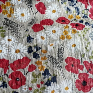 May include: A close-up of a fabric with a floral pattern. The fabric is a light beige color with red poppies, white daisies, and green leaves. The fabric has a textured, linen-like appearance.