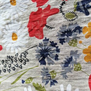 May include: A close-up of a fabric with a floral pattern. The fabric features red, white, yellow, and blue flowers on a light gray background.