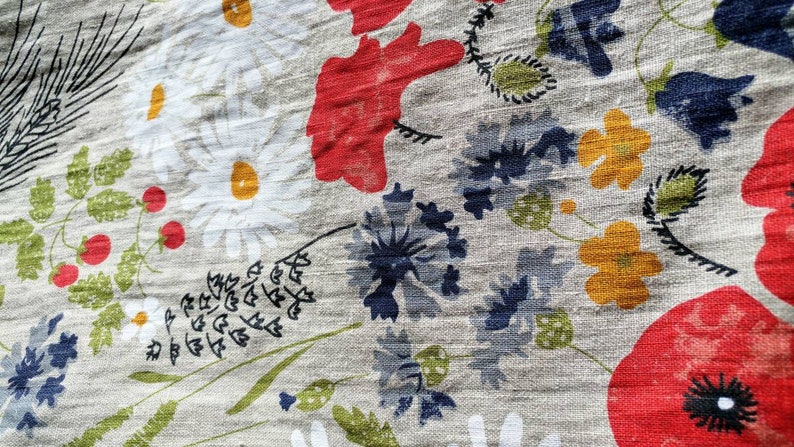 May include: A close-up of a fabric with a floral pattern. The fabric features red, white, yellow, and blue flowers on a light gray background.