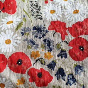 May include: A beige fabric with a repeating pattern of red poppies, white daisies, blue bells, and green leaves.
