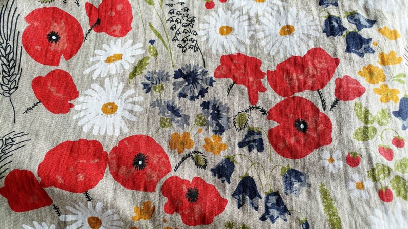 May include: A beige fabric with a repeating pattern of red poppies, white daisies, blue bells, and green leaves.