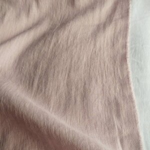 Pode incluir: Um close-up de um tecido de linho macio de cor rosa claro. O tecido est&aacute; dobrado e drapeado, mostrando sua textura e caimento.