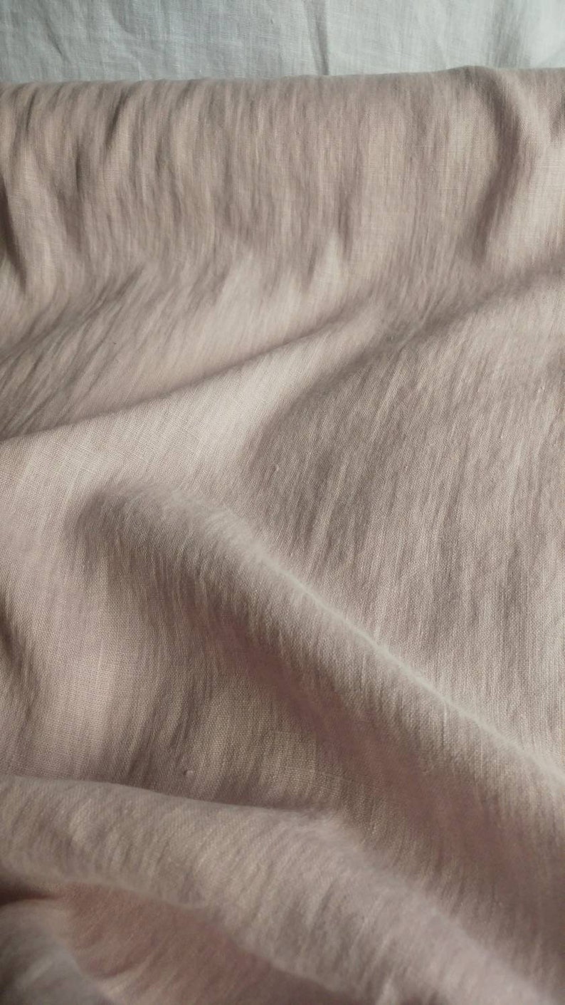 Pode incluir: Um close-up de um tecido de linho macio, rosa claro, com uma superf&iacute;cie texturizada e enrugada.