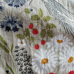 May include: A beige linen fabric with a floral pattern. The pattern includes red poppies, white daisies, bluebells, and green leaves. The fabric has a rustic and vintage feel.