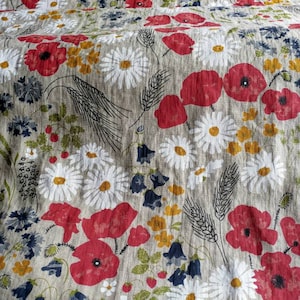 May include: A beige linen fabric with a floral pattern featuring red poppies, white daisies, and green leaves.