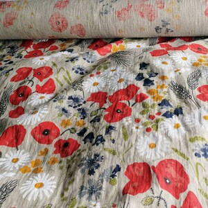 May include: A beige linen fabric with a floral print featuring red poppies, white daisies, and green foliage.