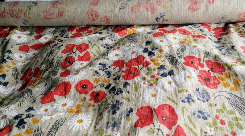 May include: A beige linen fabric with a floral print featuring red poppies, white daisies, and green foliage.