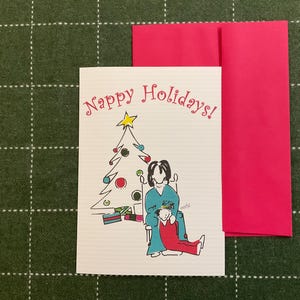 May include: A holiday greeting card with the text "Nappy Holidays!" in pink script. The card features a whimsical illustration of a Christmas tree and two figures. A bright pink envelope is included.