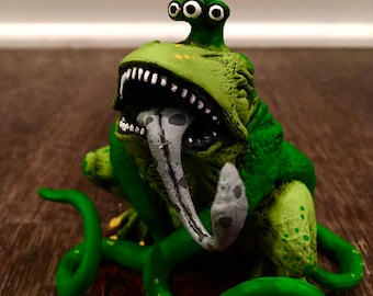 Könnte beinhalten: Grüne dreiköpfige Monsterfigur mit einem großen Maul und einer langen Zunge. Das Monster sitzt auf einer grünen Rebe mit einer braunen Basis.