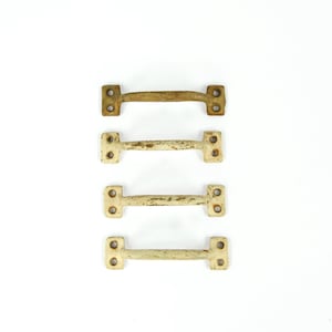 May include: Four vintage metal drawer pulls. The pulls are rectangular with a curved handle and two mounting plates with holes. The top pull is a weathered gold color, while the other three are off-white with a distressed finish.