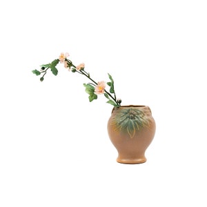 Pode incluir: Um vaso de cerâmica marrom com um design floral verde, contendo um ramo de flores rosa.
