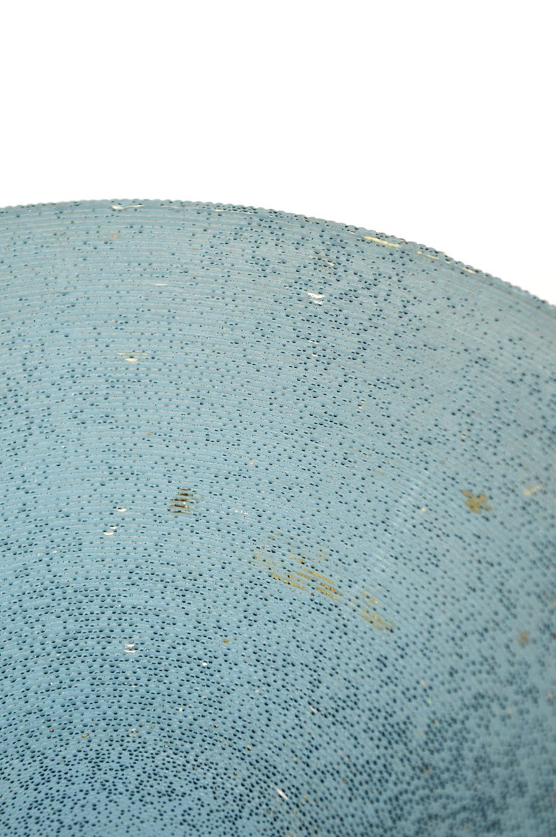 May include: Close-up of a light blue, textured surface. The surface is covered in small, dark blue dots, creating a speckled appearance. The texture appears to be slightly curved, suggesting a rounded object.