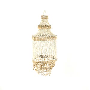 May include: A decorative hanging shell chandelier. The chandelier features a tiered design with a top section, a middle section, and a bottom section. The chandelier is made of white shells and beige-colored shells, with strands of shells hanging down.