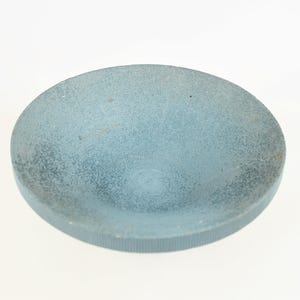 May include: A round, light blue bowl with a textured surface. The bowl has a slightly concave interior and a ridged edge. The color is a muted, dusty blue, and the bowl appears to be made of a solid material.