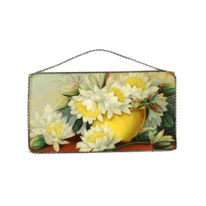 May include: Rectangular wall art featuring a floral still life. A yellow vase overflows with white flowers with yellow centers. The artwork is framed with a metal chain and has a chain for hanging.