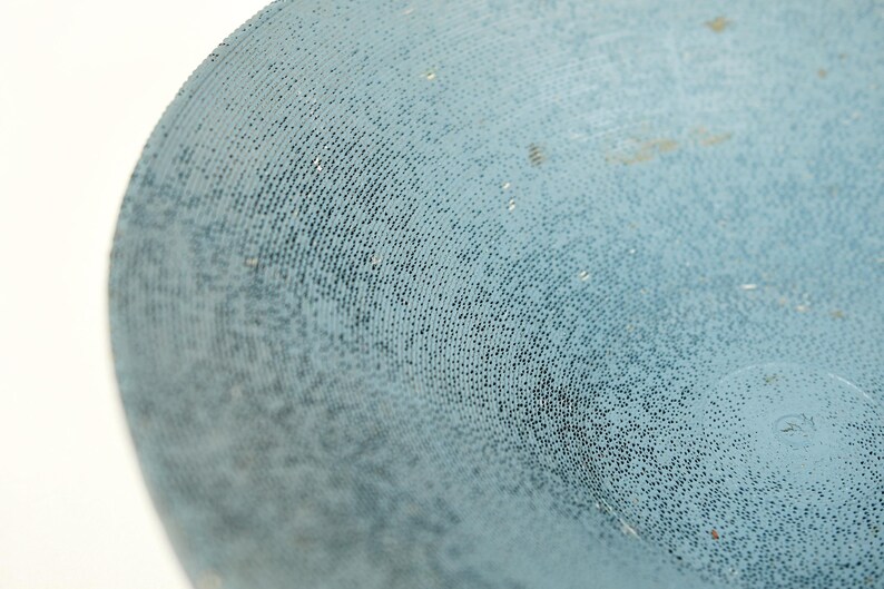 May include: Close-up of a textured, light blue surface with a pattern of small, dark dots. The surface appears to be curved, with a slight sheen. The image is well-lit, highlighting the texture.