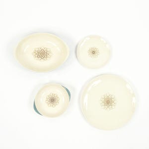 May include: Set of four white ceramic dishes with a blue rim and a brown floral design. The set includes a large oval dish, a smaller round dish, a dinner plate, and a smaller plate.