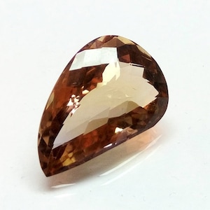 May include: A teardrop-shaped gemstone with a light brown to orange color. The gemstone is faceted and has a high polish.