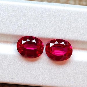 Könnte beinhalten: Zwei oval geschliffene, facettierte Rubine mit tiefroter Farbe. Die Edelsteine werden auf einer weißen Oberfläche präsentiert, die ihre brillanten Facetten und ihre satte Farbe zeigt. Ideal für die Schmuckherstellung.