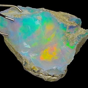 May include: A rough, natural opal gemstone with a milky white base and iridescent flashes of green, blue, orange, and yellow.
