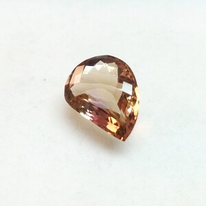 May include: A teardrop-shaped gemstone with a light brown to pink color gradient. The gemstone is faceted and has a high polish.