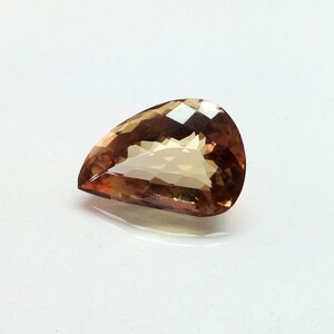 May include: A teardrop-shaped gemstone with a light brown color and a faceted cut.