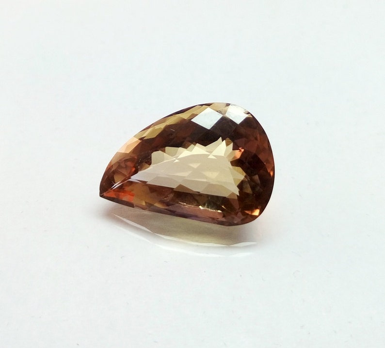 May include: A teardrop-shaped gemstone with a light brown color and a faceted cut.
