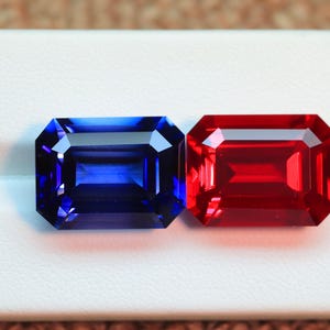 Puede incluir: Dos piedras preciosas talla esmeralda, una azul y otra roja, se muestran sobre una superficie blanca.