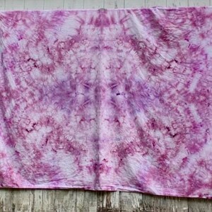 May include: A rectangular fabric piece featuring a tie-dye pattern in shades of magenta, pink, and white. The design displays a symmetrical, radial arrangement of color with intricate, crinkled textures throughout the surface of the textile.
