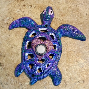 May include: A purple and green painted cast iron turtle door knocker with a white button and a pink glitter heart.