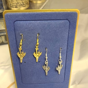 Puede incluir: Tres pares de pendientes en una tarjeta de exhibición de terciopelo azul. Los pendientes son de plata y oro y presentan un diseño de cardo.