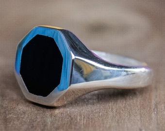 May include: A silver ring with a black octagonal stone set in a silver bezel. The ring has a polished finish.