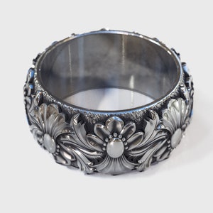 May include: A silver ring with a floral design. The ring is wide and has a smooth, polished finish.