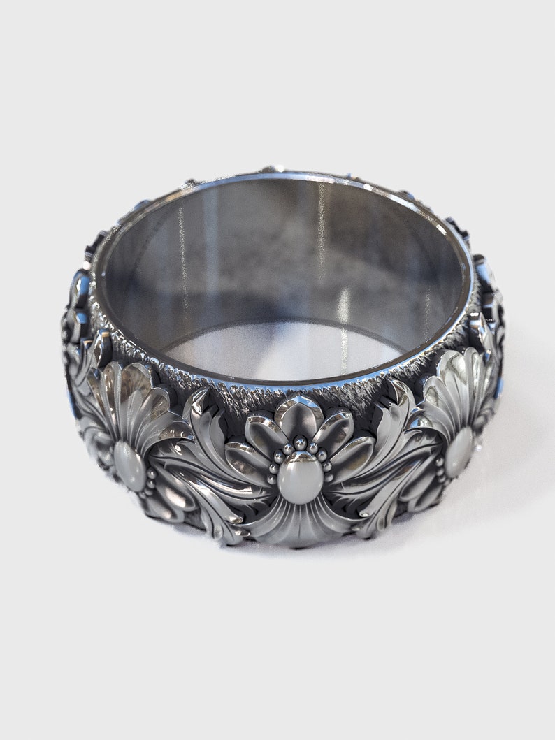 May include: A silver ring with a floral design. The ring is wide and has a smooth, polished finish.
