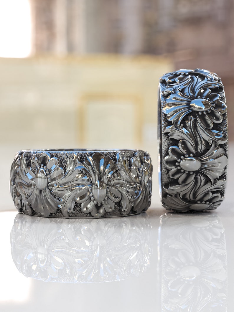 May include: Two silver rings with intricate floral designs. The rings are made of a smooth, shiny metal and have a detailed, three-dimensional pattern.