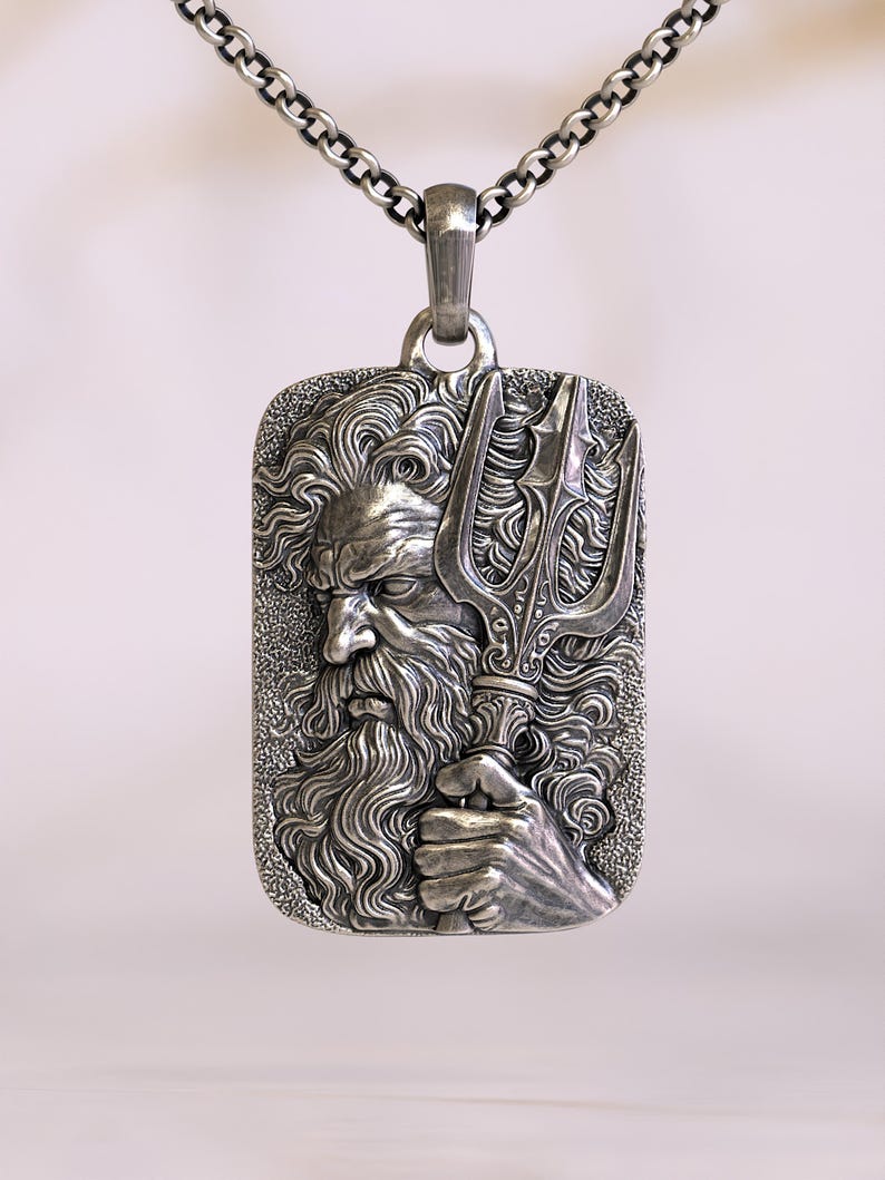 May include: A silver pendant necklace featuring a rectangular pendant with a detailed relief of a bearded man holding a trident. The pendant is attached to a silver chain. The design is intricate and the metal has a slightly aged appearance.