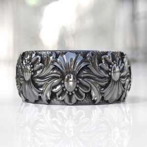 May include: A silver ring with a floral design. The ring is wide and has a textured surface.