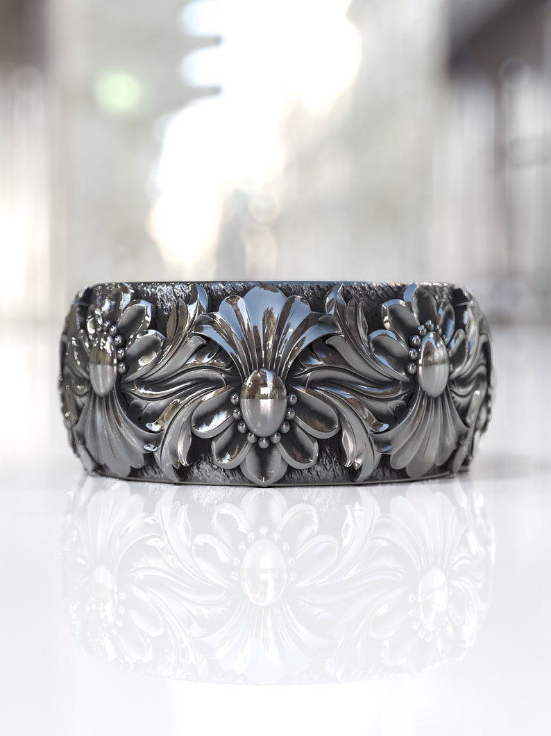 May include: A silver ring with a floral design. The ring is wide and has a textured surface.