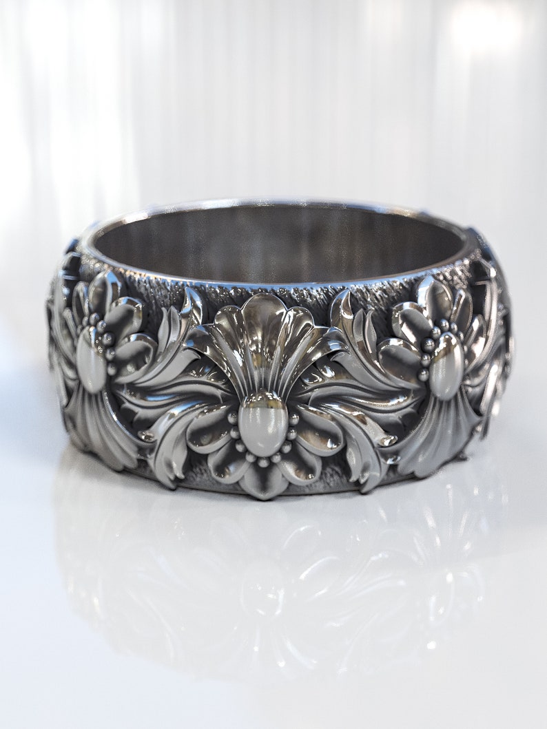 May include: A silver ring with a floral design. The ring is wide and has a polished finish.
